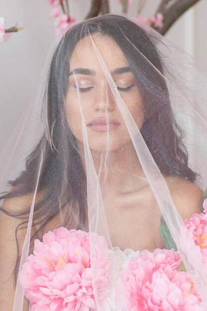 Retrato vertical de una joven sentada en una bañera bajo el tul y sosteniendo un ramo de flores Foto de alta calidad