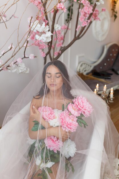 Retrato vertical de una joven sentada bajo tul con flores en la bañera Foto de alta calidad