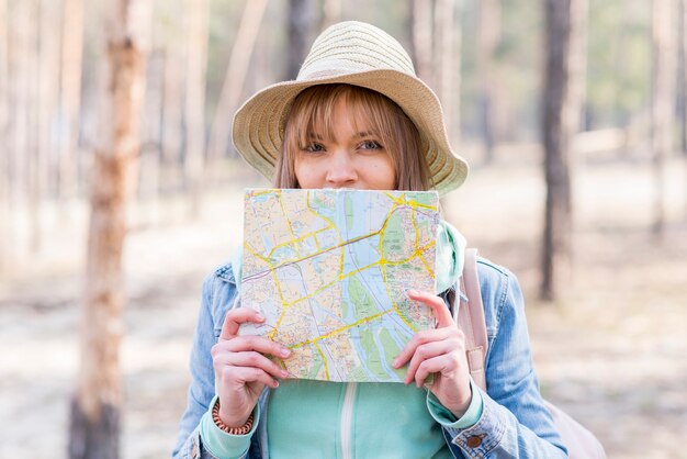Retrato de un viajero femenino que sostiene un mapa delante de su boca mirando a la cámara