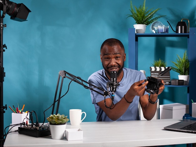 Retrato de un videógrafo que presenta un cabezal de trípode fluido para grabar video en un estudio de vlogging. Vlogger que explica las características del dispositivo de estabilización de video con sistema de liberación rápida.