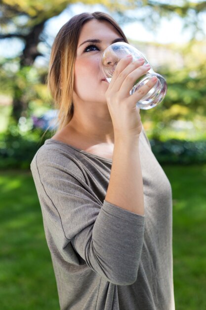 Retrato del vidrio de agua potable de la muchacha hermosa en el parque verde.