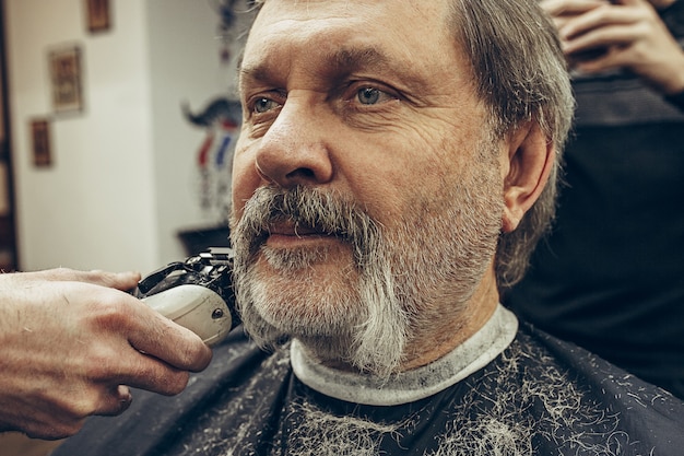 Retrato de vista lateral de primer plano de guapo hombre caucásico barbudo senior conseguir barba aseo en la moderna barbería.