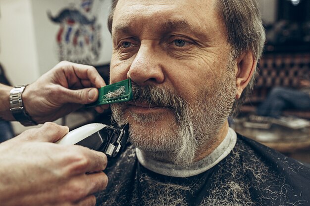 Retrato de vista lateral de primer plano de guapo hombre caucásico barbudo senior conseguir barba aseo en la moderna barbería.