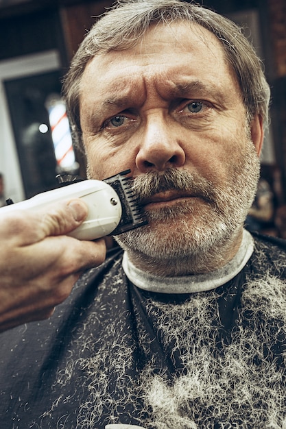 Retrato de vista lateral de primer plano de guapo hombre caucásico barbudo senior conseguir barba aseo en la moderna barbería.