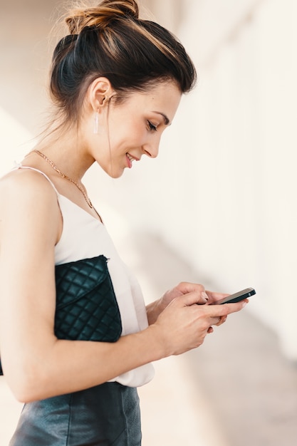 Retrato de vista lateral de una sonriente joven elegante usando un teléfono inteligente