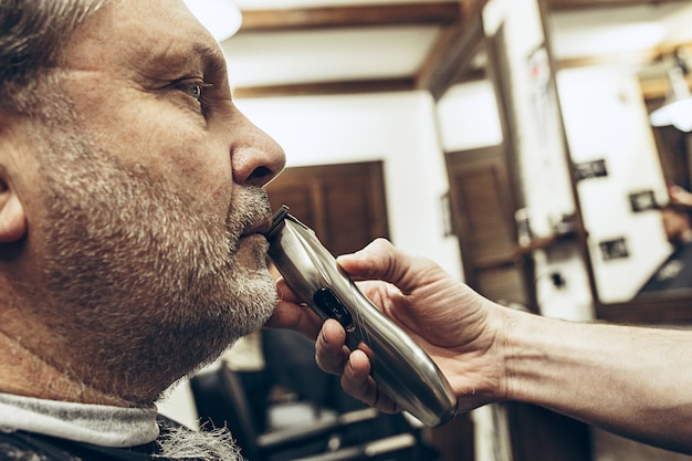 Retrato de vista de perfil lateral de primer plano de hombre caucásico barbudo senior guapo conseguir barba aseo en la barbería moderna.