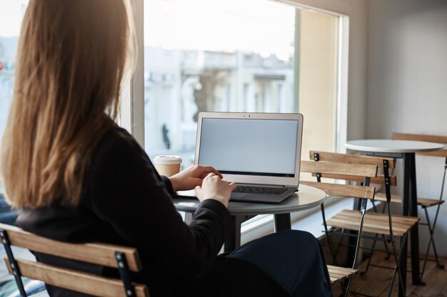 Retrovisor de exitosa mujer independiente en ropa elegante sentado en la cafetería mientras trabajaba en la computadora portátil