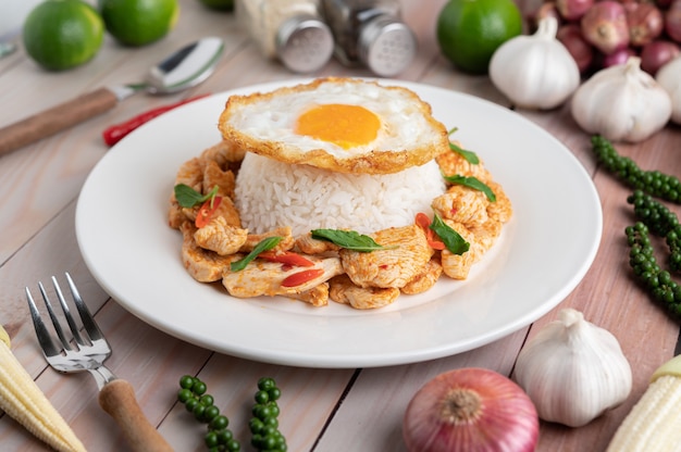Revuelva pollo frito con pasta de chile con arroz Huevos fritos en plato blanco sobre mesa de madera.