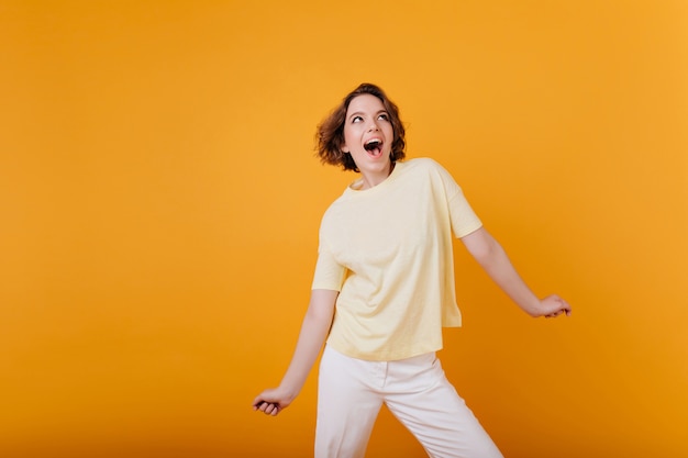 Riendo a chica increíble con tatuaje posando en la pared de color naranja brillante. hermosa dama europea en traje casual de moda.