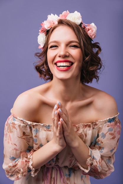 Riendo a la chica de moda posando en vestido romántico. Fascinante modelo femenino rizado en diadema de flores que expresa emociones positivas.