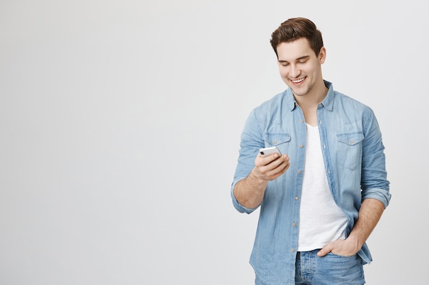 Foto gratuita riendo feliz chico sonriendo al teléfono móvil, mensajería