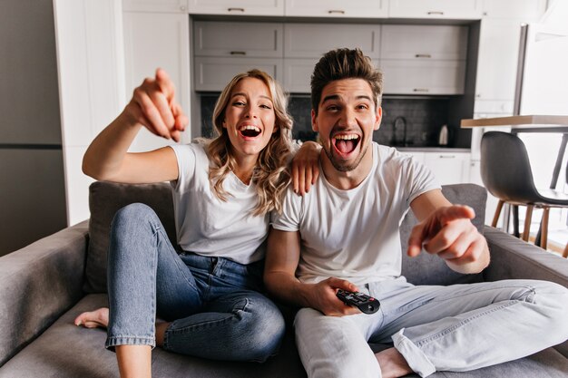 Riendo a los jóvenes sentados en el sofá. Familia sonriente viendo la televisión.