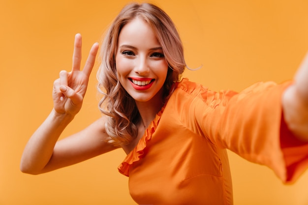Riendo a mujer alegre en vestido naranja tomando una foto de sí misma