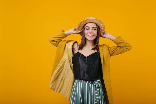 Riendo a mujer atractiva en sombrero de paja posando. Señora atractiva en negro sin mangas aislado.