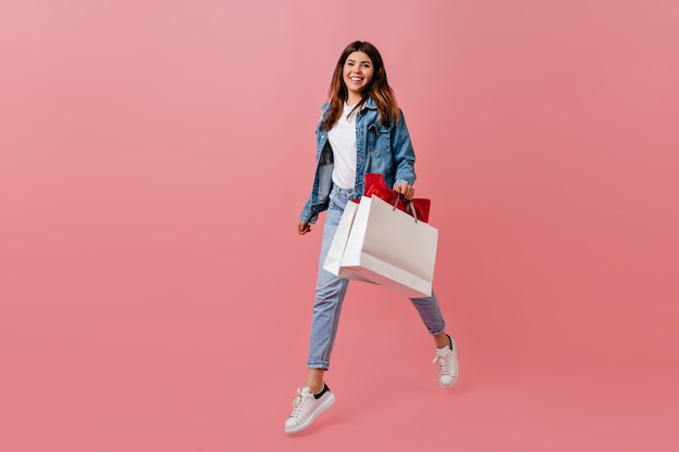 Riendo a mujer bonita con bolsa de tienda. Chica en ropa de mezclilla posando sobre fondo rosa.