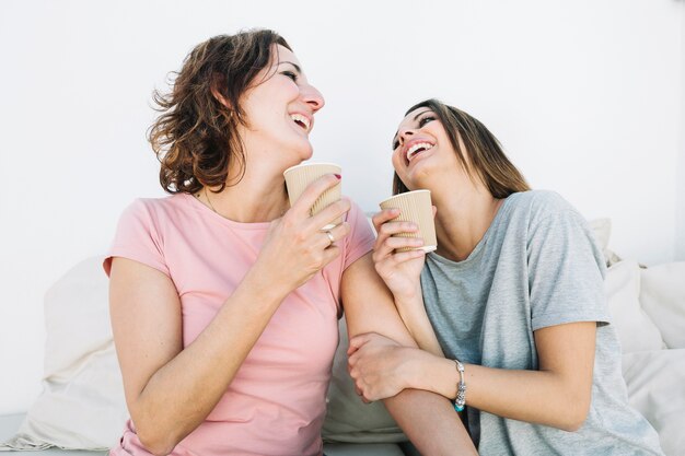 Riendo a mujeres bebiendo bebidas calientes en el sofá