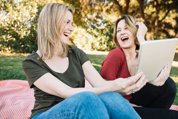 Riendo a las mujeres que usan la tableta en el parque