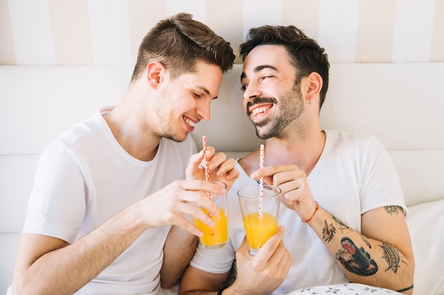 Riendo pareja gay disfrutando de jugo en la cama