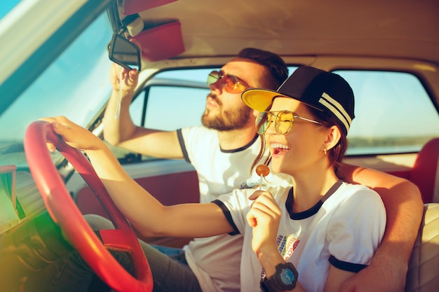 Riendo pareja romántica sentada en el coche mientras está en un viaje por carretera en verano