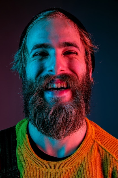 Foto gratuita riendo, sonriendo, de cerca. retrato de hombre caucásico sobre fondo de estudio degradado en luz de neón. hermoso modelo masculino con estilo hipster. concepto de emociones humanas, expresión facial, ventas, publicidad.