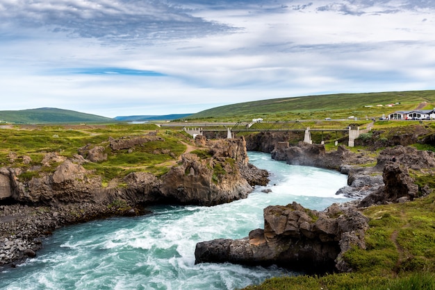 Un río desde las cataratas de Godafoss, Akureyri, Islandia, rodeado de enormes rocas y un puente de hormigón.