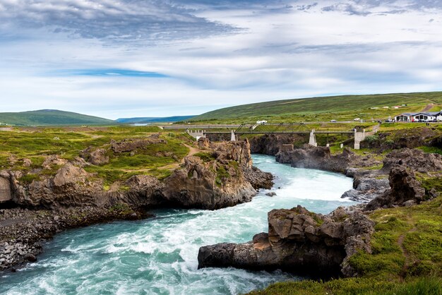 Un río desde las cataratas de Godafoss, Akureyri, Islandia, rodeado de enormes rocas y un puente de hormigón.