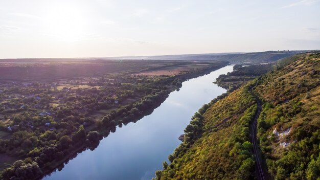 Río que fluye entre una colina con pendiente cubierta de vegetación y pueblo