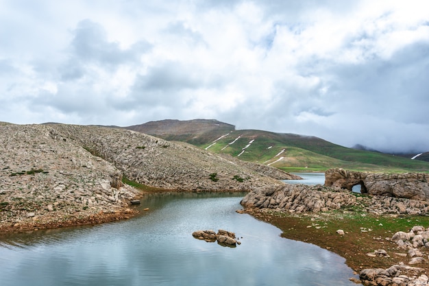 Río que fluye a través de colinas rocosas. día nublado