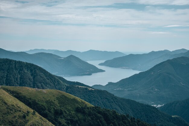 Río rodeado de colinas cubiertas de bosques y niebla bajo el cielo nublado y la luz del sol