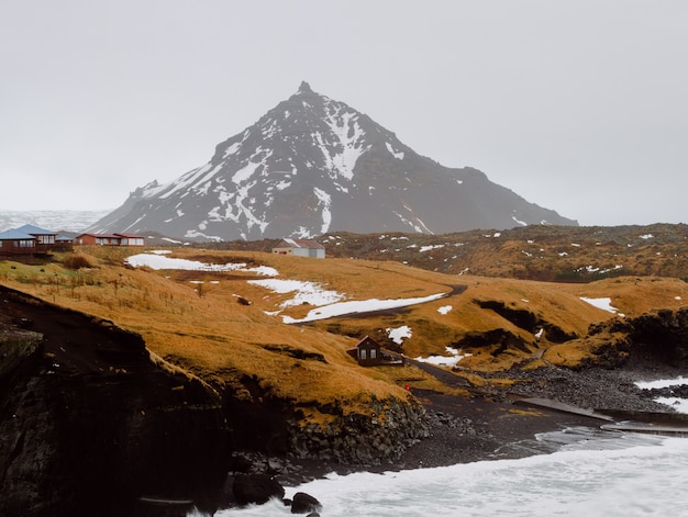 Foto gratuita río rodeado de rocas y colinas cubiertas de nieve y hierba en una aldea de islandia