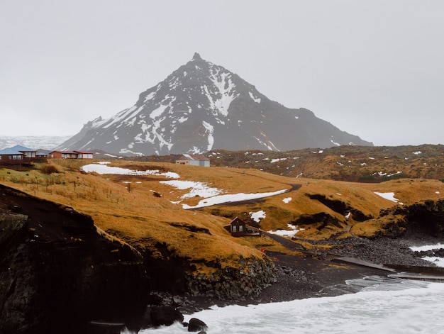 Río rodeado de rocas y colinas cubiertas de nieve y hierba en una aldea de Islandia