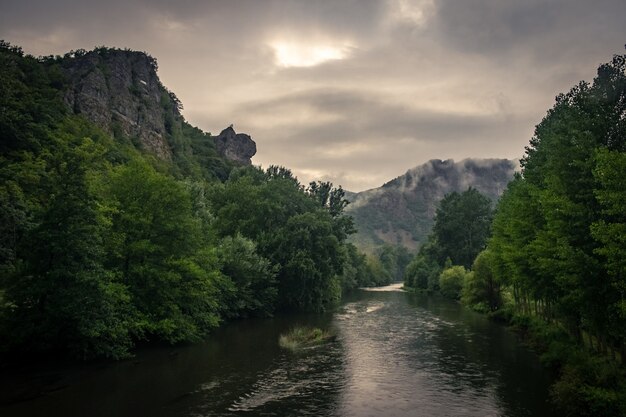 Río rodeado de rocas cubiertas de musgo y bosques bajo la luz del sol y un cielo nublado