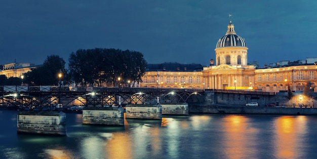 Río Sena con Pont des Arts y panorama del Institut de France por la noche en París, Francia.