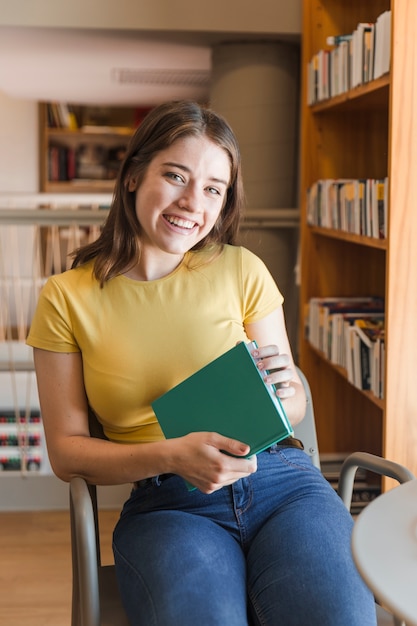 Foto gratuita risa adolescente con libro en la biblioteca