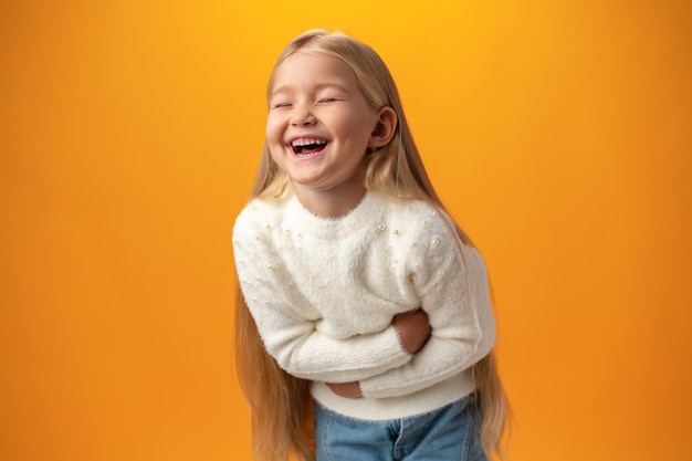 Risa alegre de una niña rubia con fondo amarillo en el estudio