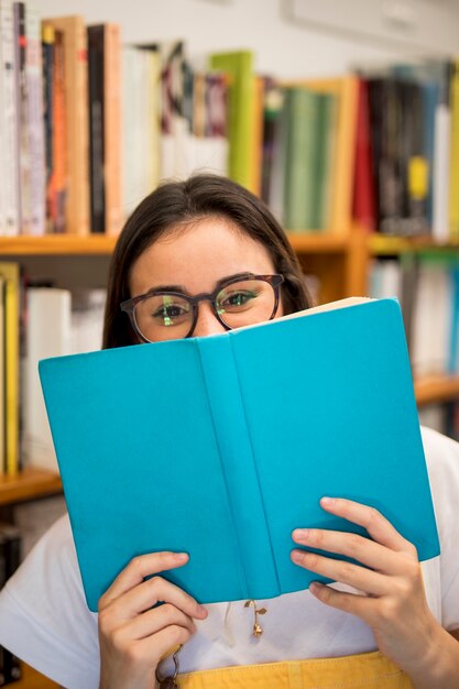 Risa colegiala adolescente que cubre la cara con el libro