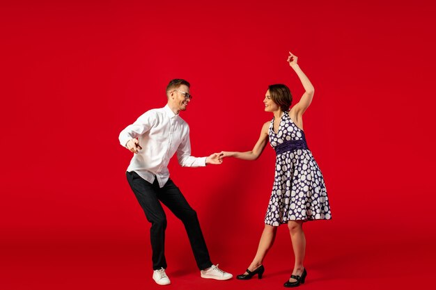 Rock and roll. Baile de la mujer joven pasada de moda de la vieja escuela aislado en fondo rojo del estudio. Hombre y mujer con estilo joven.