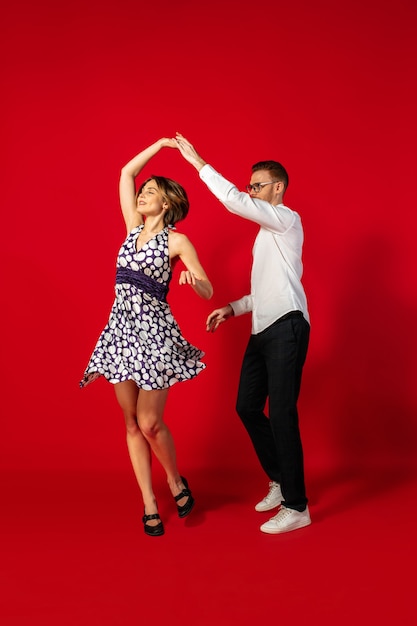 Rock and roll. Baile de la mujer joven pasada de moda de la vieja escuela aislado en fondo rojo del estudio. Hombre y mujer con estilo joven.