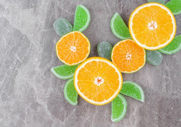 Rodajas de caramelos jugosos de mermelada de naranja y verde sobre la superficie de mármol.