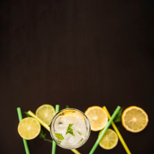 Rodajas de cítricos junto a vaso de bebida con hielo.