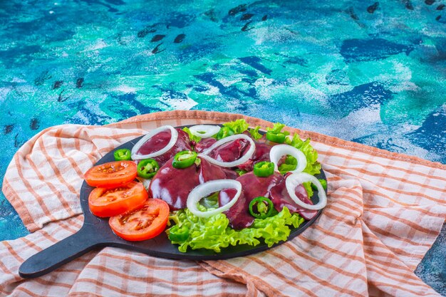 Rodajas de diversas verduras e hígados de pollo en la tabla de cortar sobre el paño de cocina