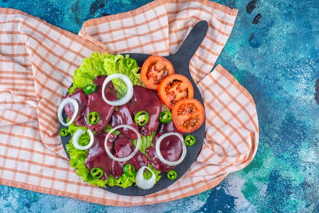 Rodajas de diversas verduras e hígados de pollo en la tabla de cortar sobre el paño de cocina