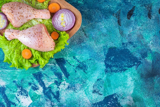 Rodajas de diversas verduras y muslos de pollo marinados en la tabla de cortar