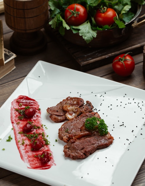 Rodajas de filete de cordero con cereza de cornalina y salsa en plato cuadrado blanco