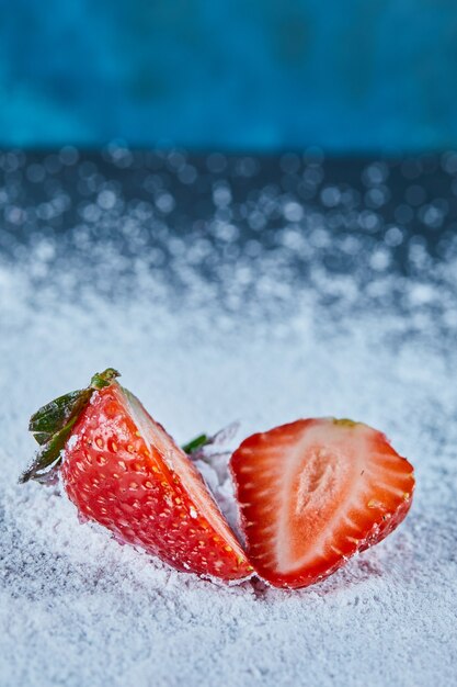 Rodajas de fresa fresca sobre superficie azul con polvo