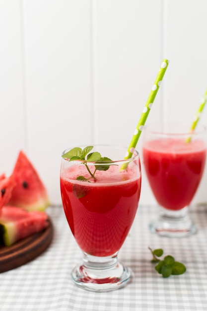 Rodajas de frutas a bordo y vasos con cóctel en servilleta cerca de las plantas