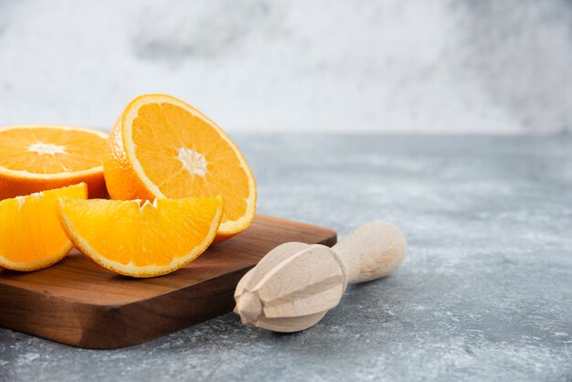 Rodajas de frutas de naranja con un escariador de madera sobre una tabla de madera.