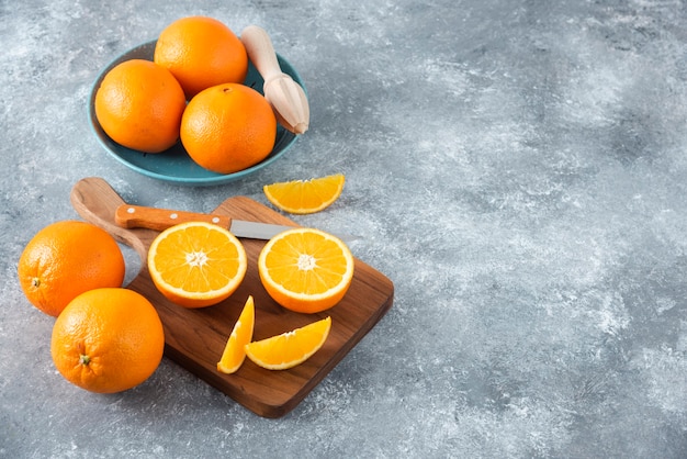 Rodajas de frutas de naranja con naranjas enteras sobre una tabla de madera.