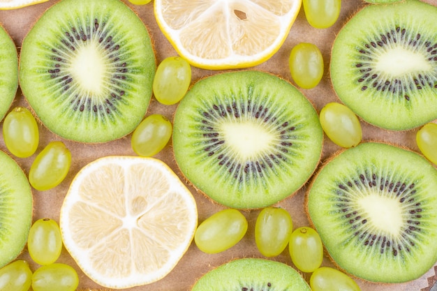 Rodajas de kiwi fresco, uvas y limón sobre tabla de cortar de madera.