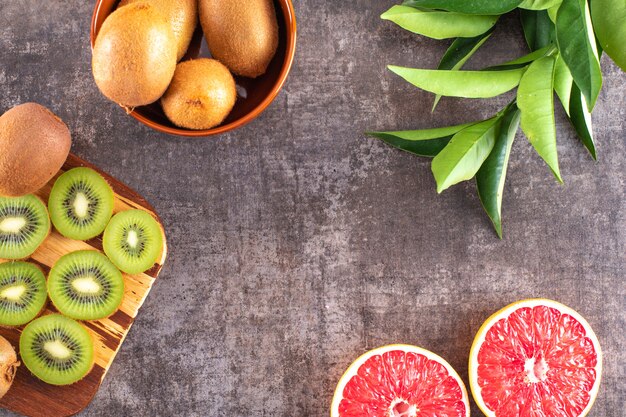 Rodajas de kiwi en un tazón de tabla de cortar lleno de kiwi rodajas de pomelo en superficie gris